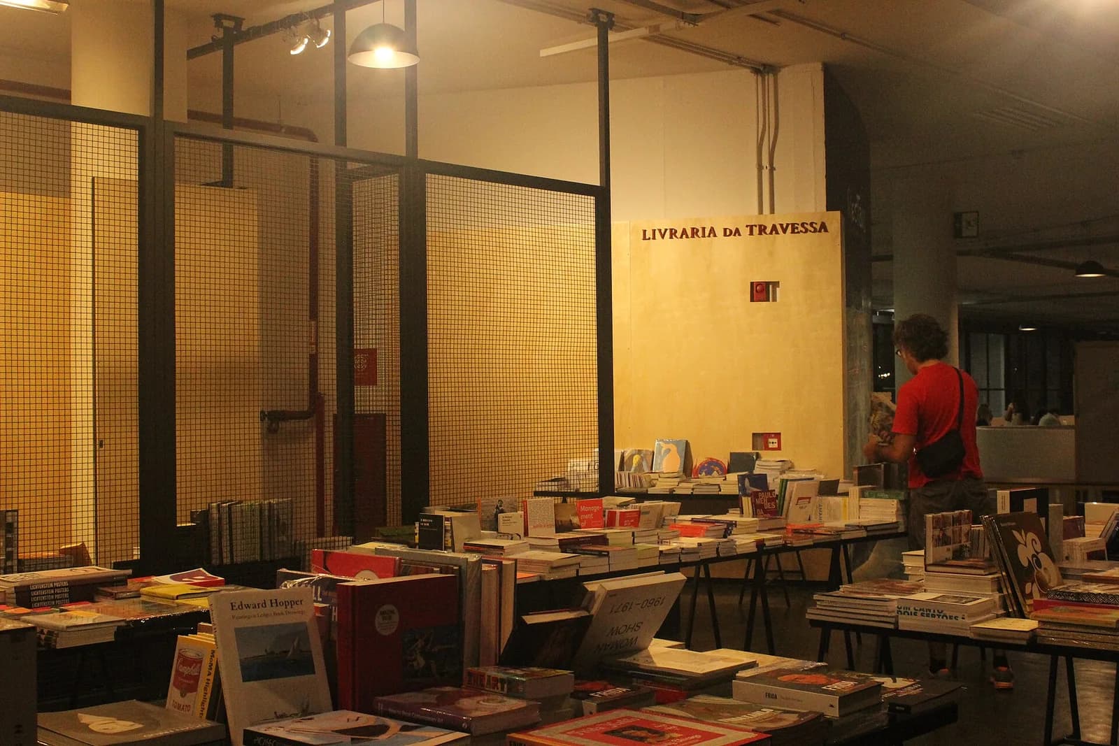 Mesas com livros expostos em uma livraria montada dentro de um pavilhão de feira